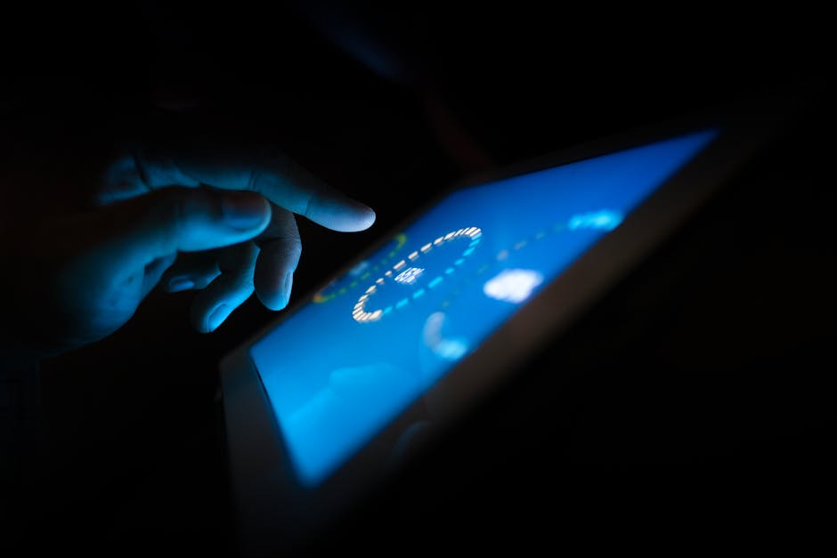 Close-up of a hand interacting with a glowing touchscreen in a dark setting.